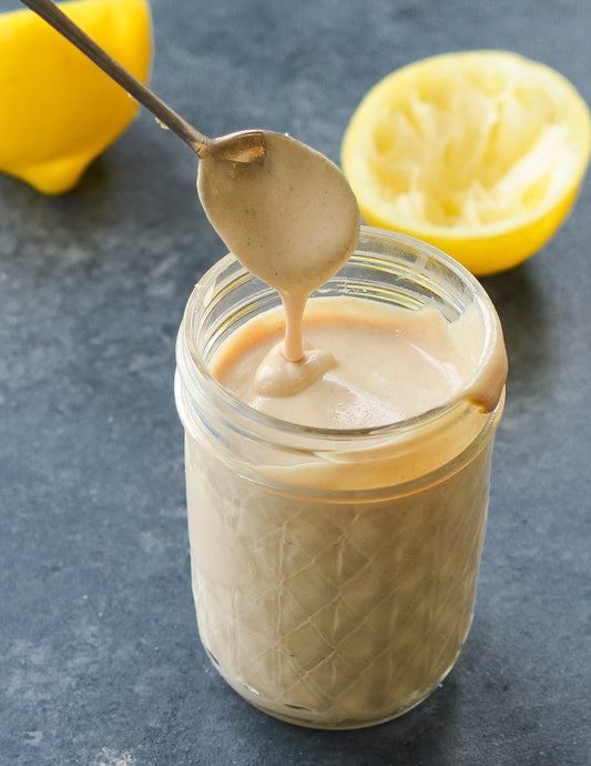 FUN Sesames Tahini Sauce | Chilled tahini in a jar, nestled in the refrigerator, with a vibrant lemon in the background, ready to elevate your dishes with its creamy texture and zesty flavor.