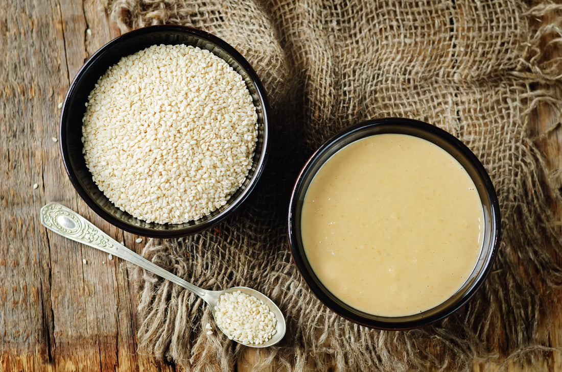 FUN Sesames Tahini Paste | Two black bowls—one with tahini paste, the other with sesame seeds—accompanied by a spoon, capturing the essence of this versatile ingredient.