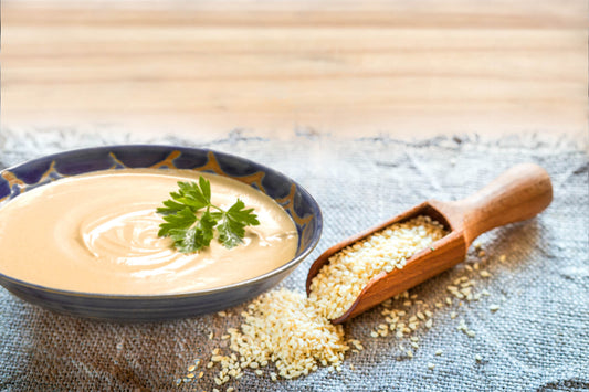 FUN Sesames Tahini Sauce | Sesame sauce topped with parsley in a bowl, accompanied by a wooden spoon of sesame seeds.